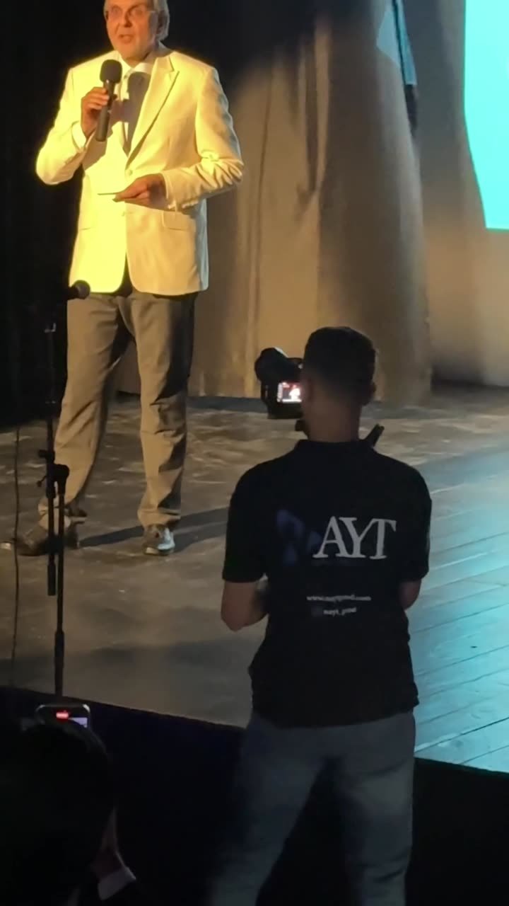 Opérateur en t-shirt NAYT filmant un intervenant au micro sur scène.